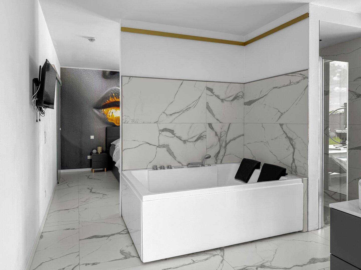 Elegantes Badezimmer mit Badewanne und offenem Zugang zum stilvoll eingerichteten Schlafzimmer.