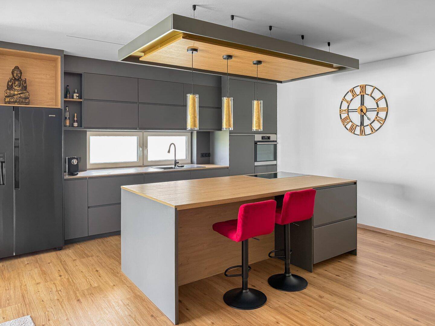 Moderne Küche mit grauen Schränken, Holztheke und Kücheninsel mit roten Barhockern.