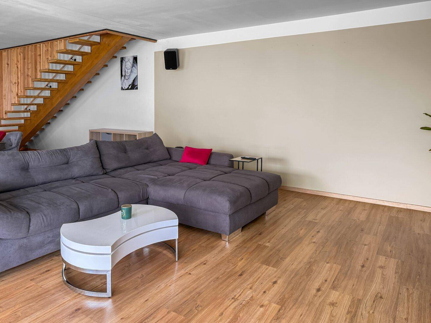 Helles Wohnzimmer mit grauem Sofa, modernem Couchtisch und offener Holztreppe.