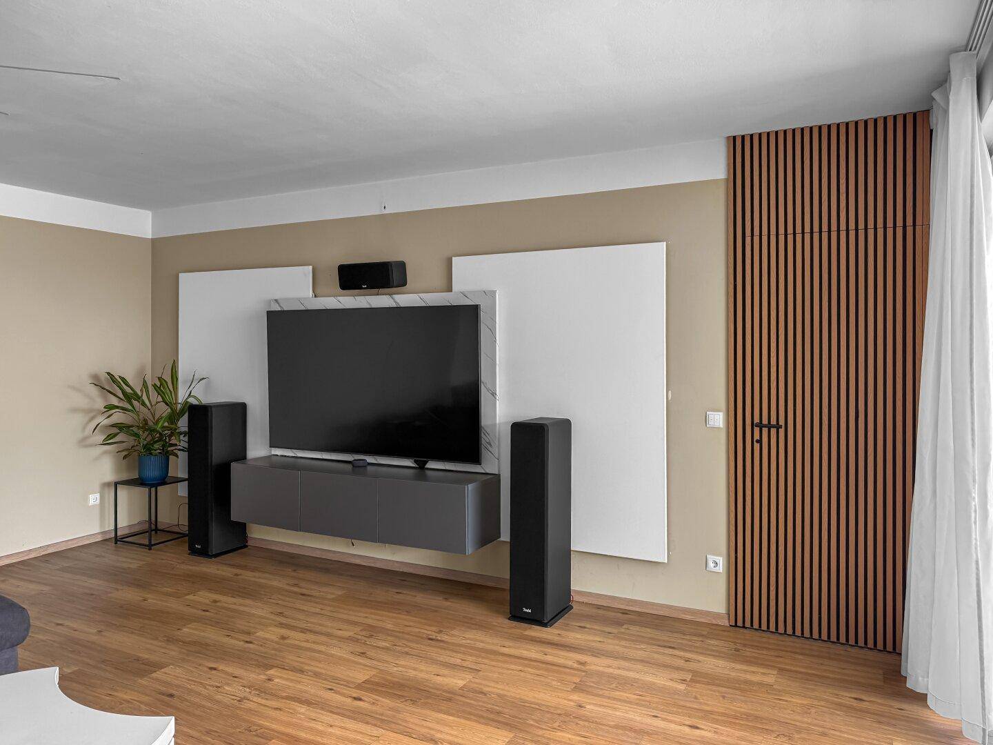 Wohnzimmerwand mit großem Fernseher, Soundsystem und dekorativer Holzlamellenverkleidung.