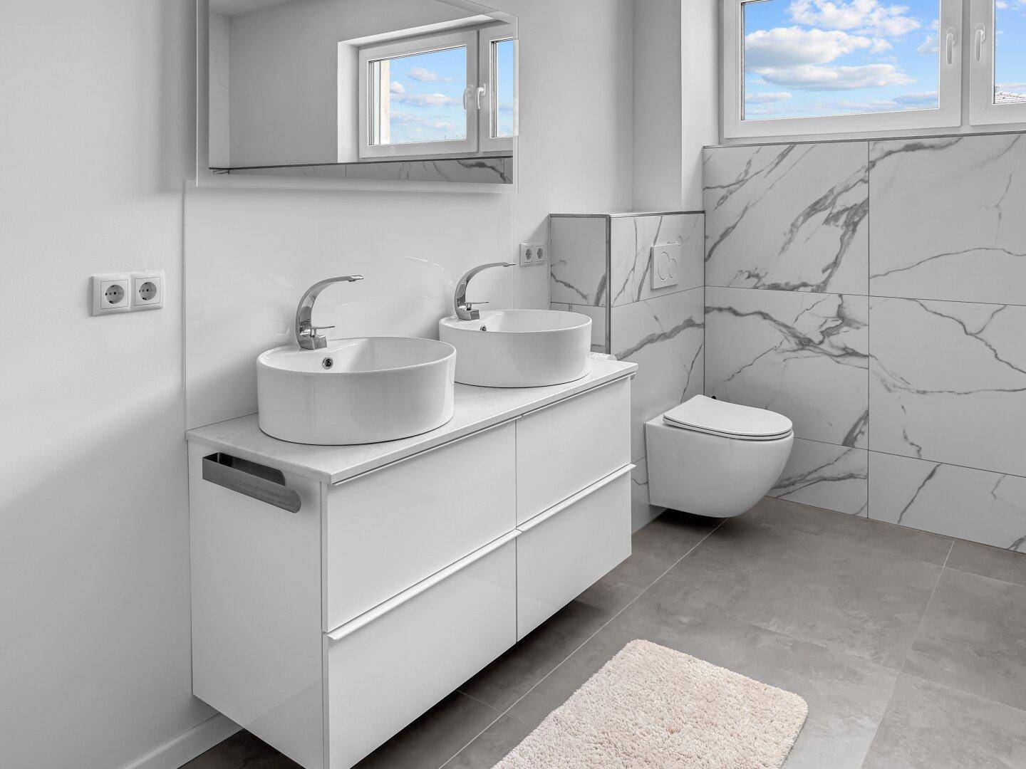Helles Badezimmer mit Doppelwaschbecken, Wand-WC und Fenster für natürliches Licht.