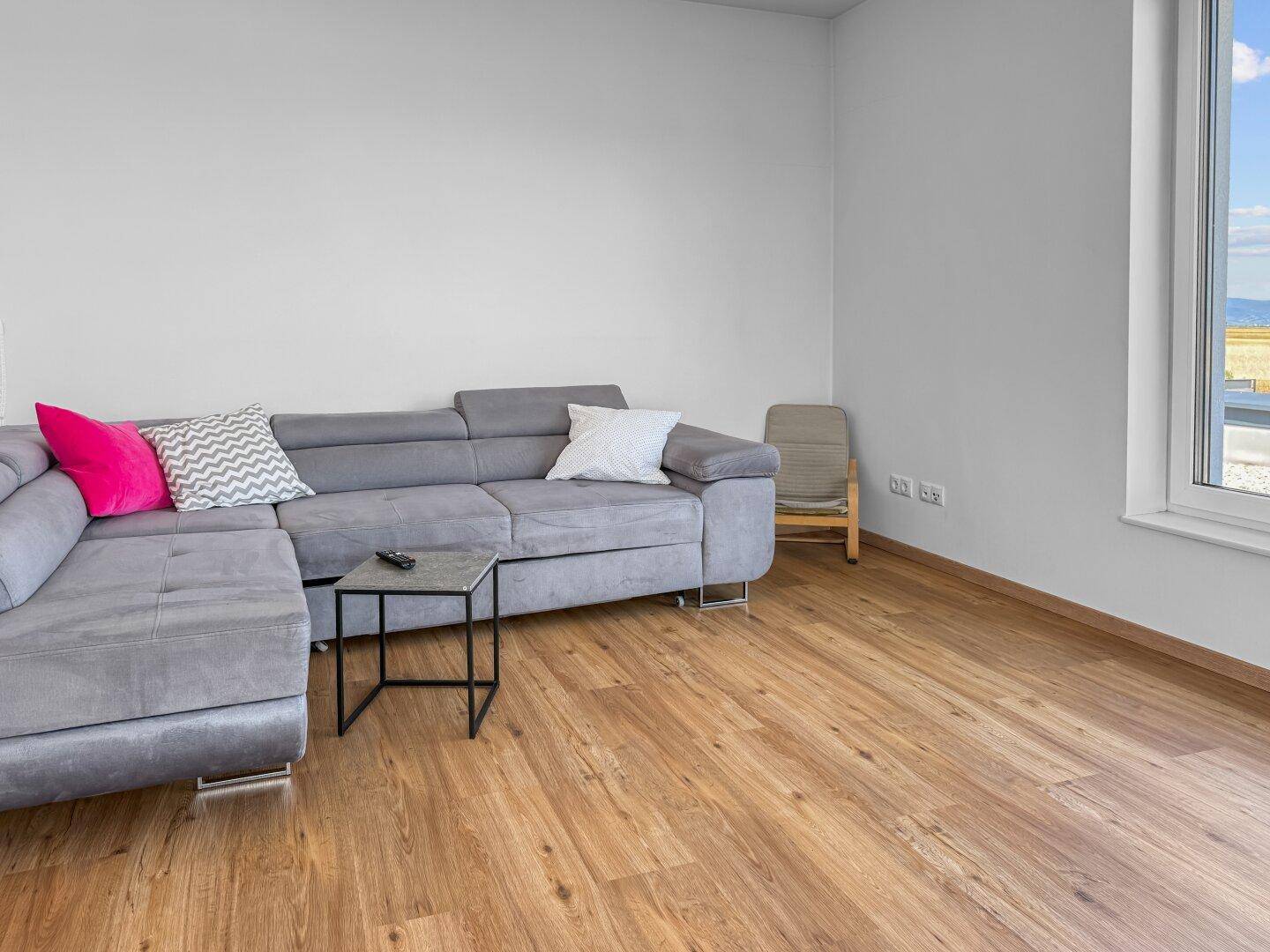 Geräumiges Wohnzimmer mit grauem Ecksofa, Holzboden und großen Fenstern.