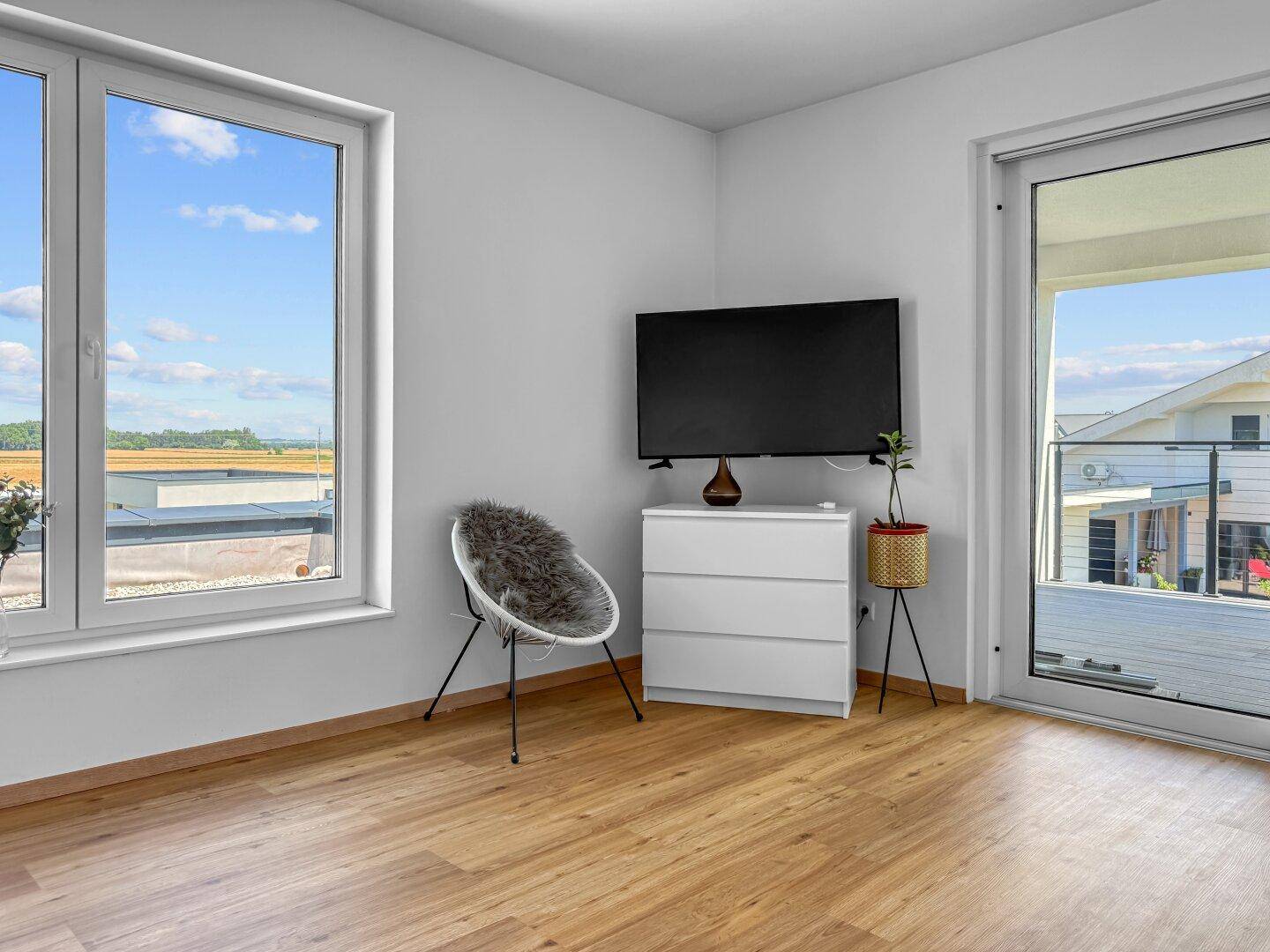 Helles Wohnzimmer mit Holzboden, Wandfernseher und Zugang zur Terrasse.