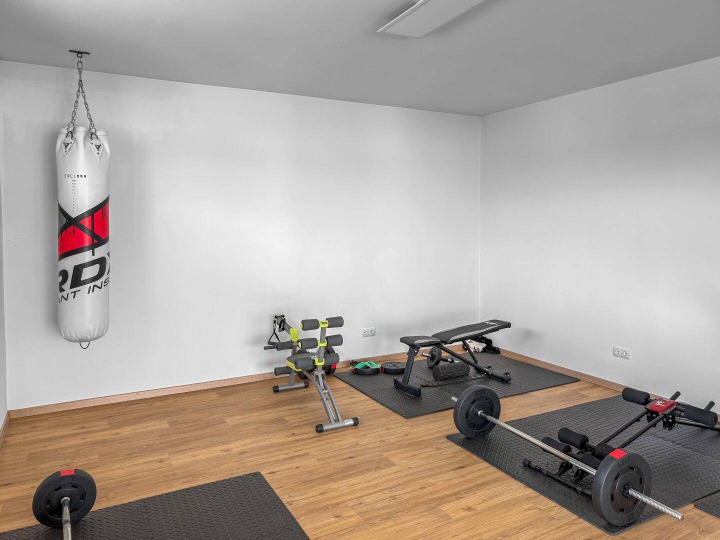 Privater Fitnessraum mit Boxsack, Hanteln und Trainingsgeräten auf Holzboden.
