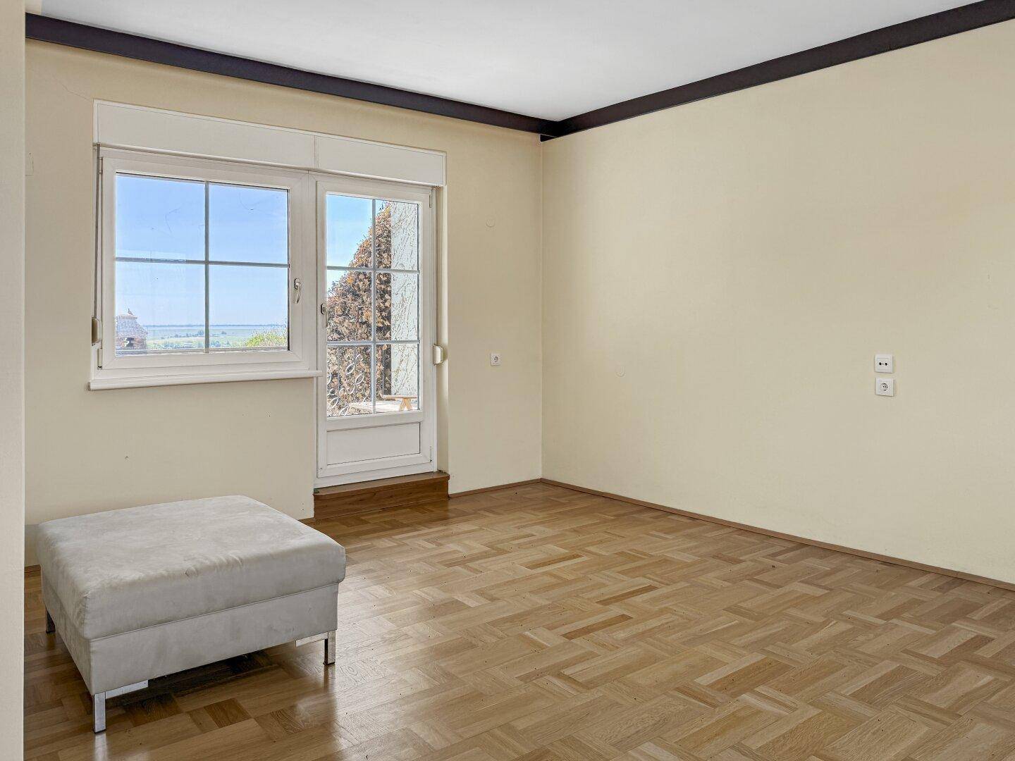 Schlafzimmer mit Fischgrätparkett und Zugang zu einem Balkon, bietet eine weite Aussicht.
