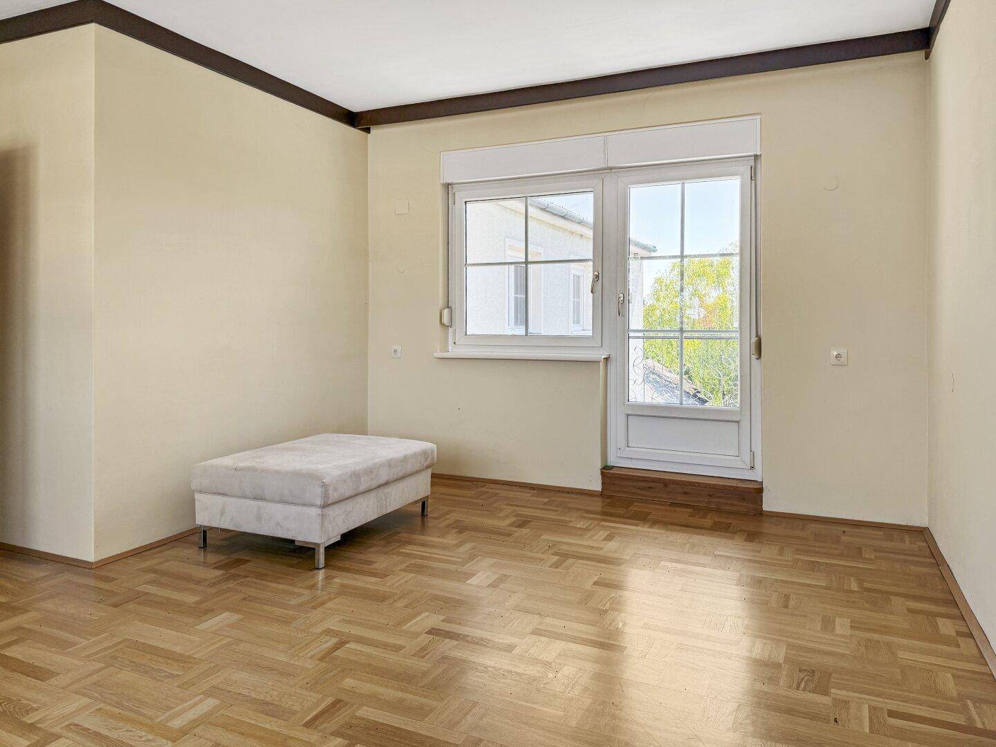 Schlafzimmer mit hellem Parkettboden und Tür zum Balkon, ideal für frische Luft.