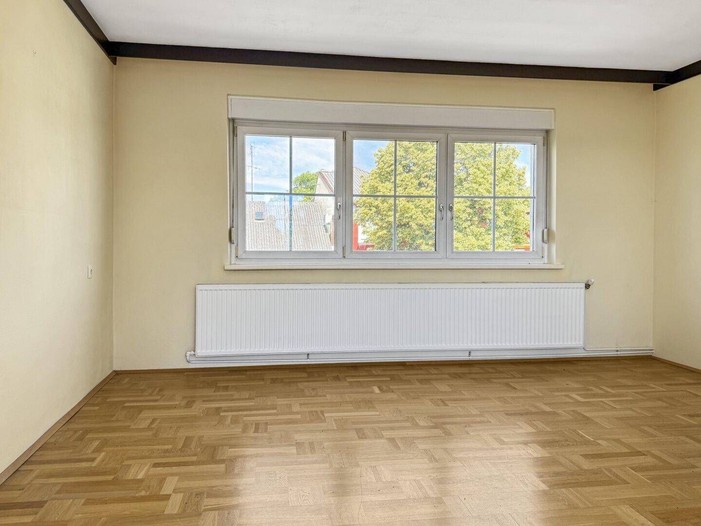Helles Schlafzimmer mit großem Fenster und Heizkörper, bietet Blick auf die Umgebung.
