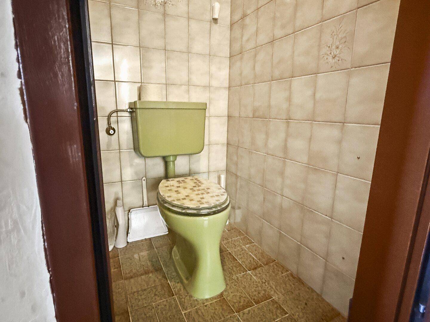 Separate Toilette mit grünem WC und Fliesen im 80er-Jahre-Design.