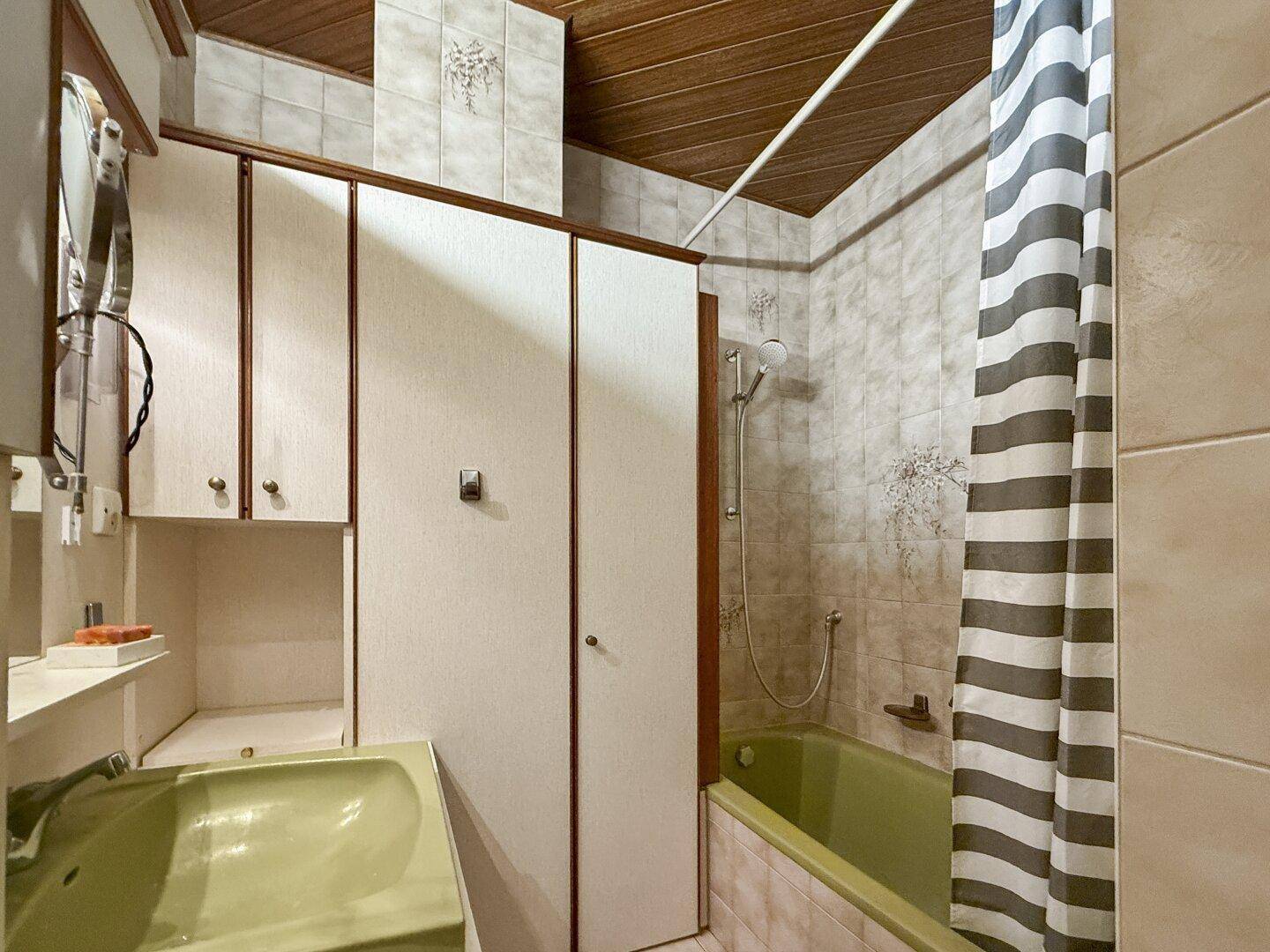 Badezimmer mit grüner Badewanne, Duschvorhang und Holzdecke im Retro-Stil.