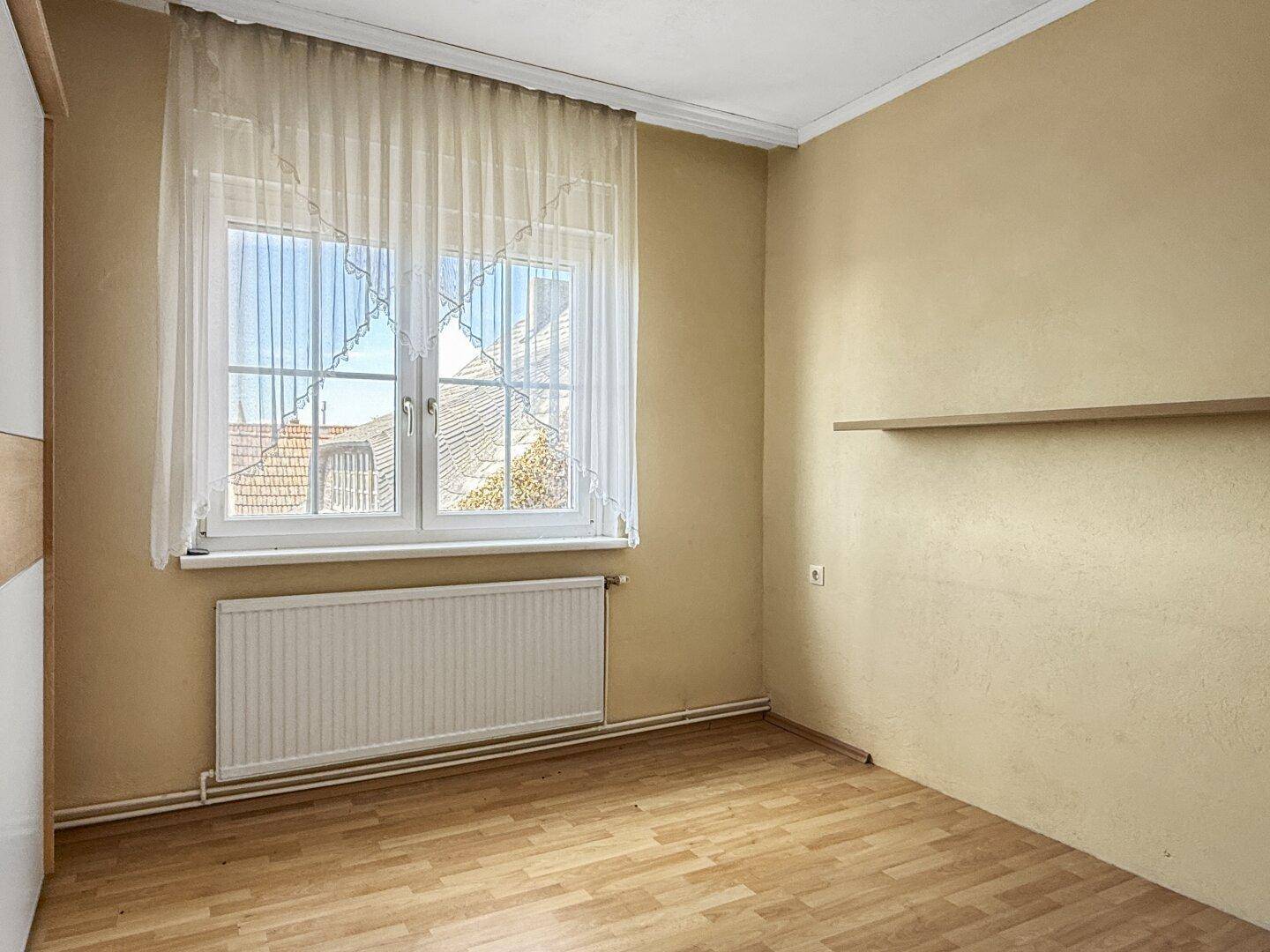 Schlafzimmer mit Laminatboden und einem Fenster, das den Raum mit Tageslicht versorgt.