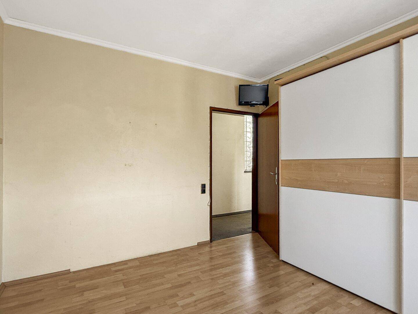 Schlafzimmer mit Laminatboden und Zugang zu einem weiteren Raum, ausgestattet mit einem Schrank.