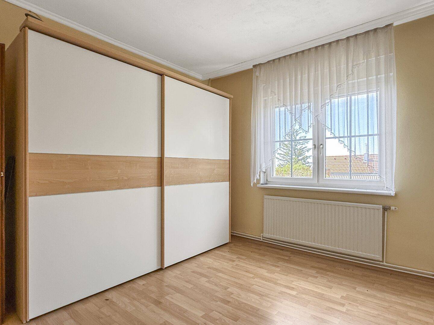 Schlafzimmer mit großem Einbauschrank und Laminatboden, bietet viel Stauraum.