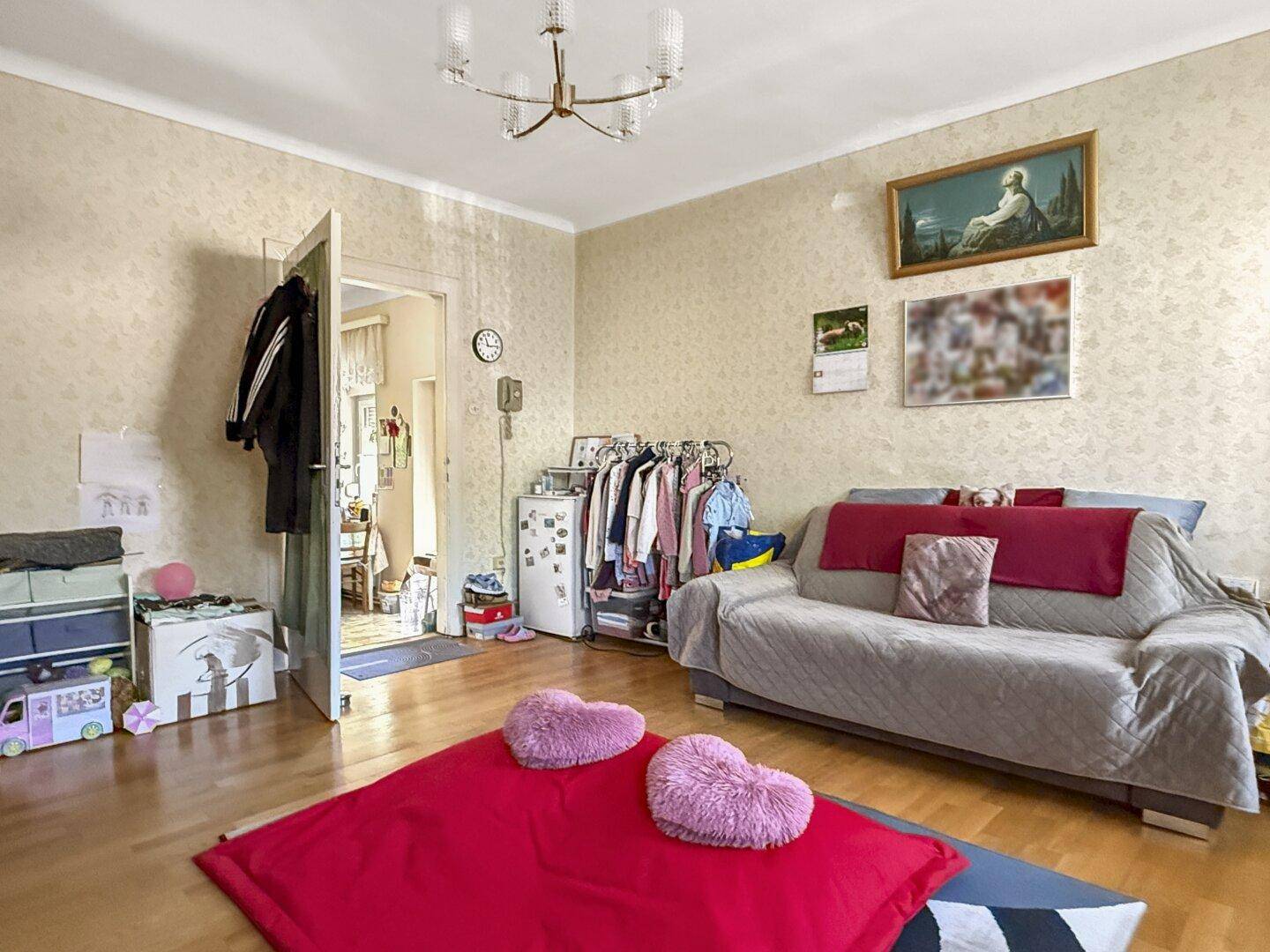 Gemütliches Wohnzimmer mit Sofa, Holzboden und Zugang zu einem weiteren Raum.