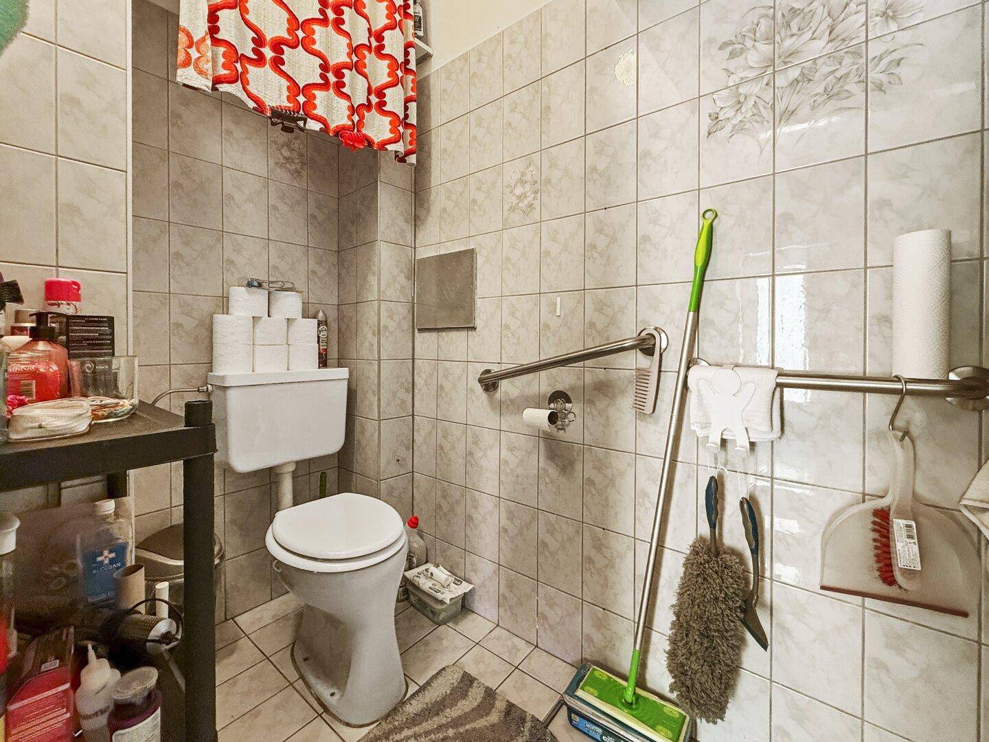 Badezimmer mit WC, Haltegriffen und Fliesen im hellen Design.