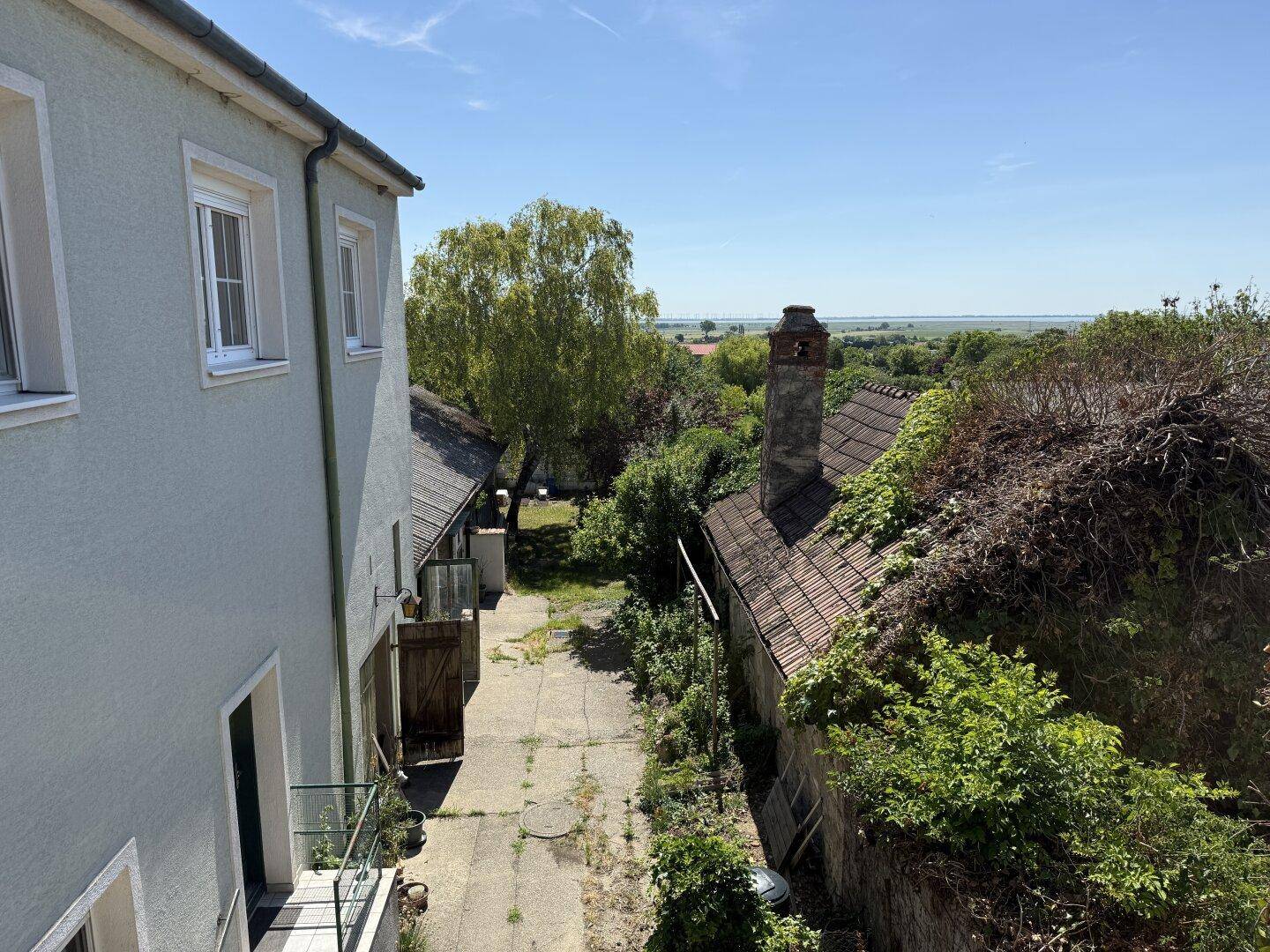 Blick vom Gebäude auf den Hofbereich mit Nebengebäuden und weite Landschaft im Hintergrund.