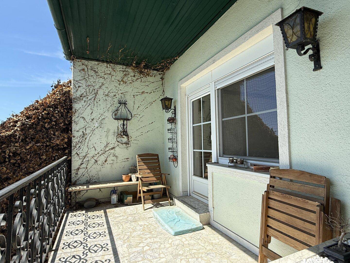 Überdachter Balkon mit Fliesenboden und schmiedeeisernem Geländer, bietet Platz zum Entspannen.