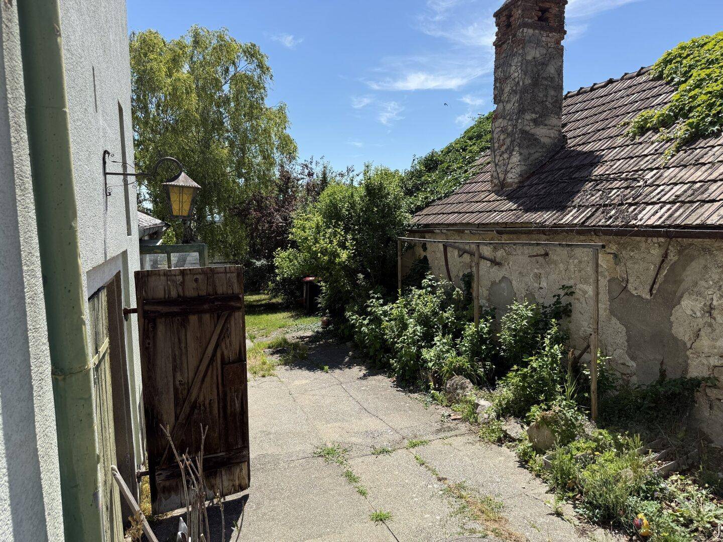 Alter Hofbereich mit Kopfsteinpflaster, üppiger Vegetation und einem historischen Schornstein.