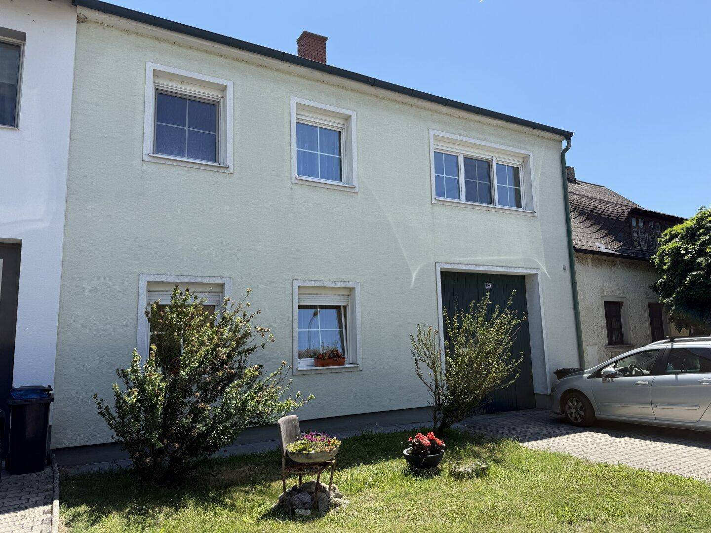 Fassade des Hauses mit mehreren Fenstern und einem Garagentor, umgeben von Grünflächen.