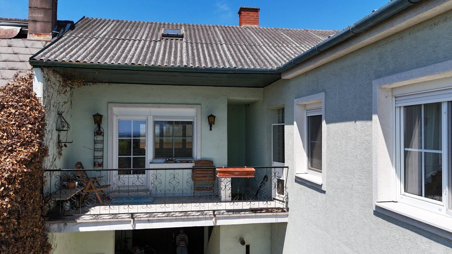 Balkon mit schmiedeeisernem Geländer, Sitzgelegenheiten und Blick auf das Dach des Hauses.