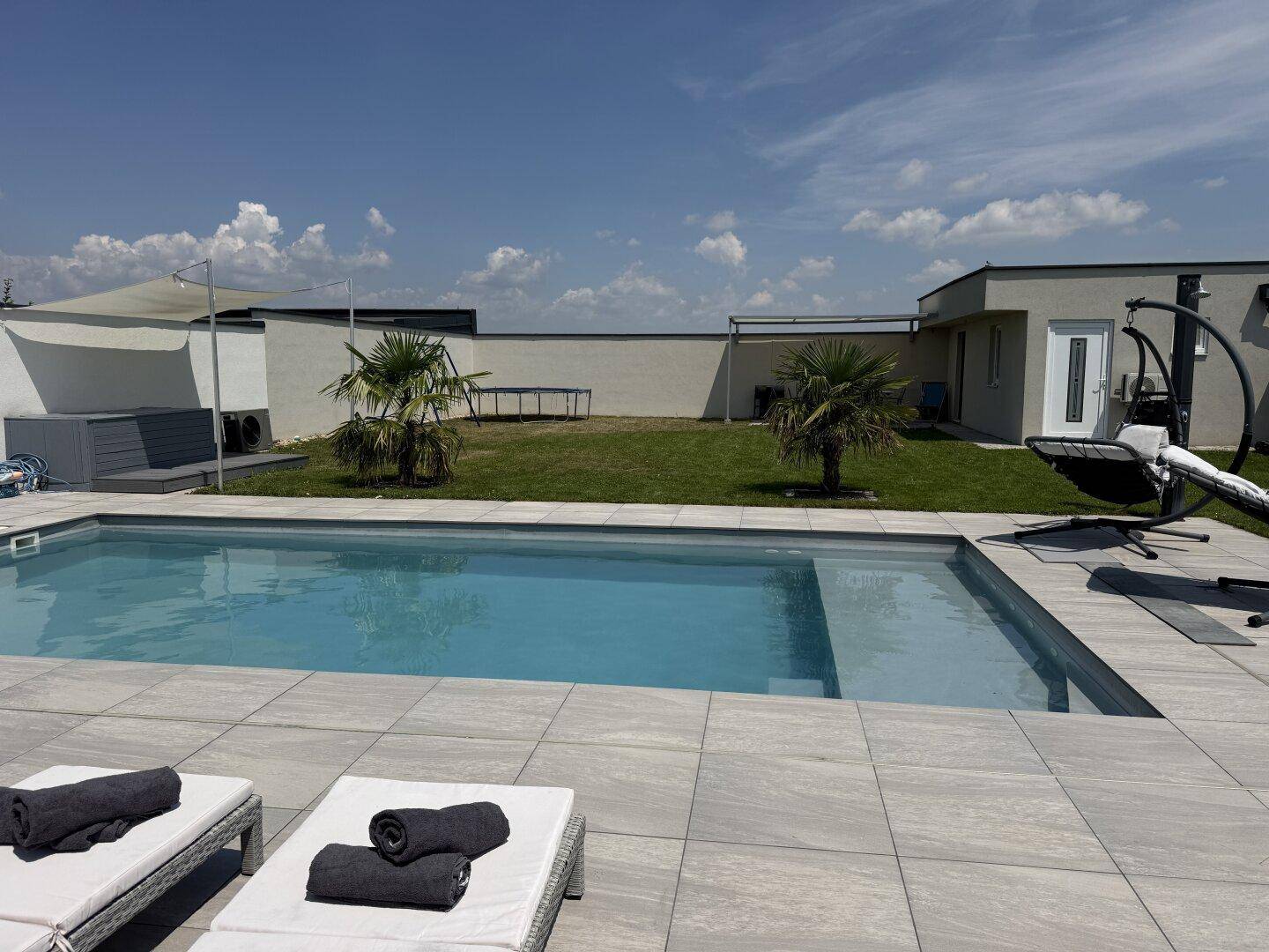 Moderner Außenbereich mit Pool, Liegestühlen und Palmen unter blauem Himmel.