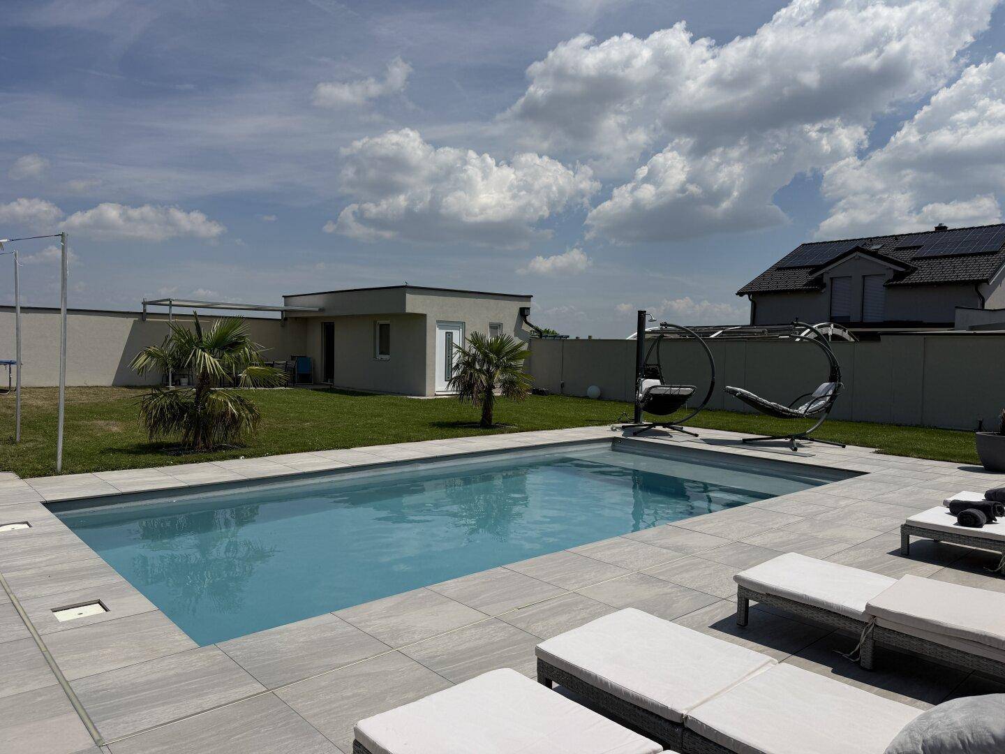 Weitläufiger Garten mit Pool, Liegeflächen und moderner Architektur im Hintergrund.