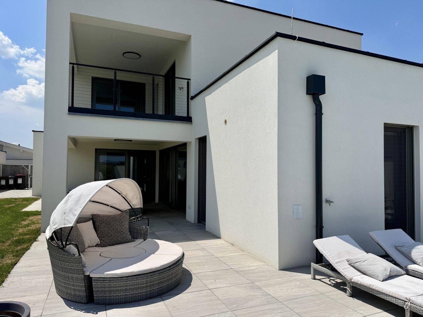 Moderne Hausfassade mit großer Terrasse und bequemen Outdoor-Möbeln.