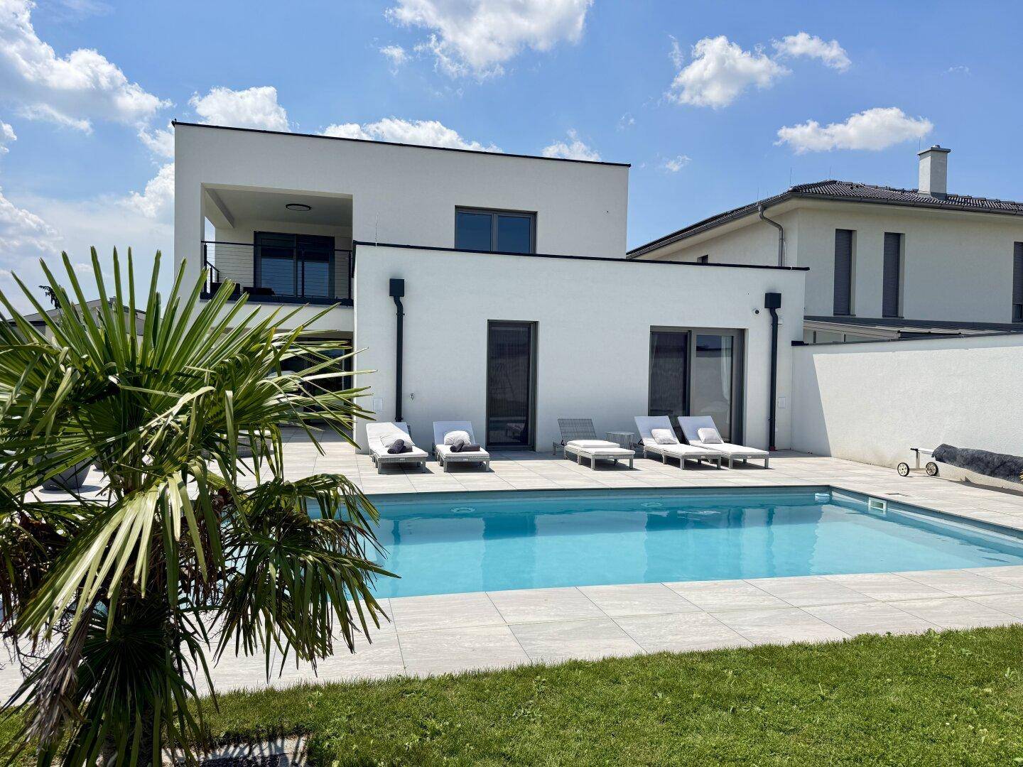 Zeitgenössische Villa mit großem Swimmingpool, Liegestühlen und gepflegtem Rasenbereich.