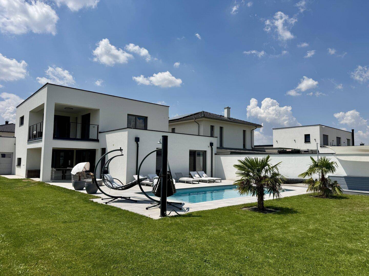 Weitläufiger Garten mit Pool, Liegeflächen und moderner Architektur im Hintergrund.