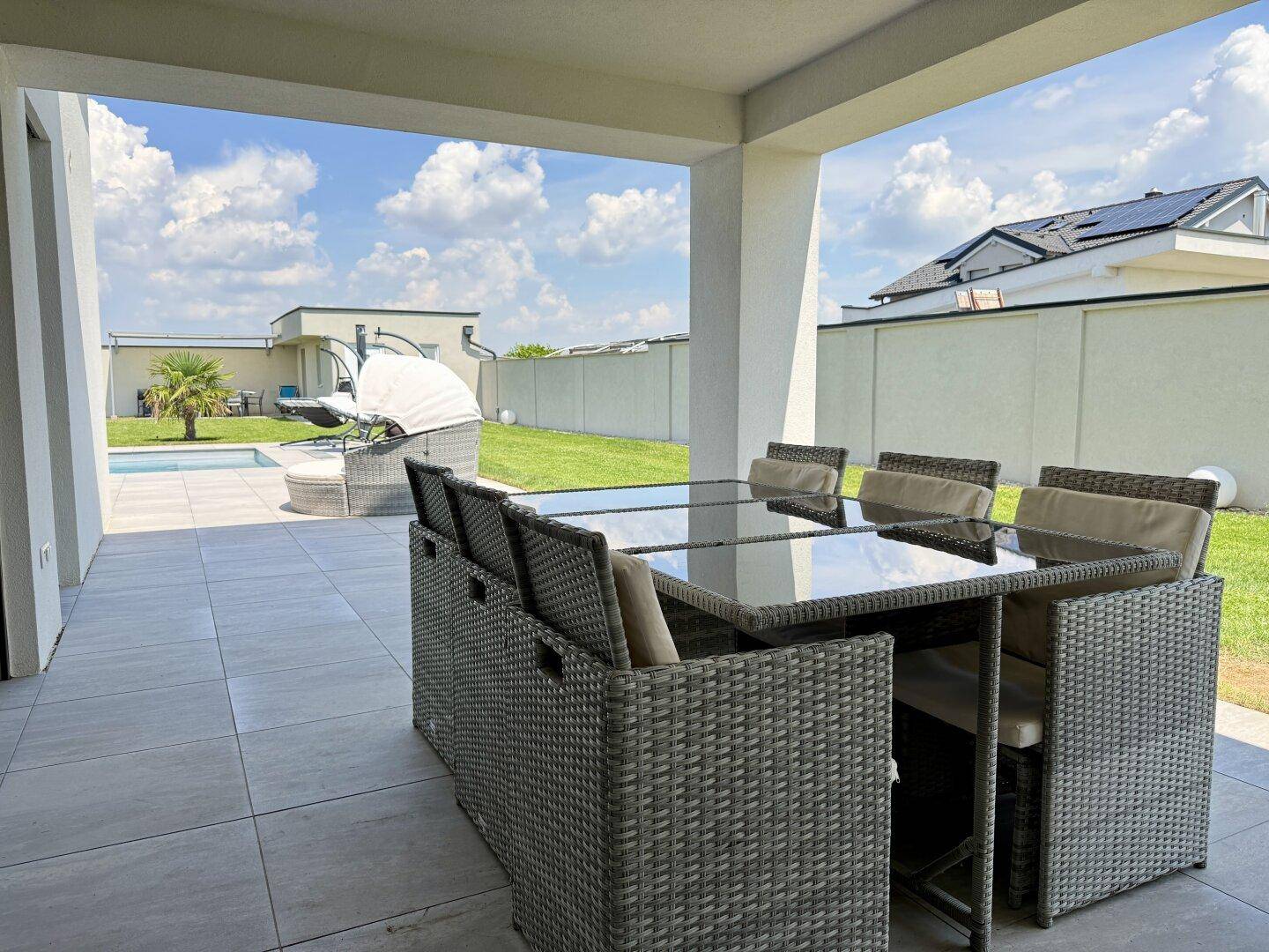 Überdachte Terrasse mit großem Esstisch und Zugang zum Garten und Poolbereich.