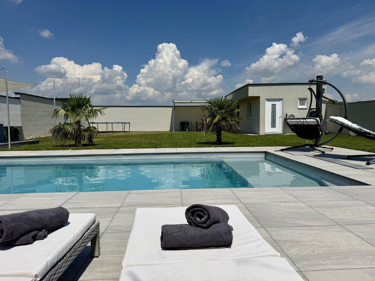 Entspannungsbereich am Pool mit bequemen Liegestühlen und blauem Himmel.
