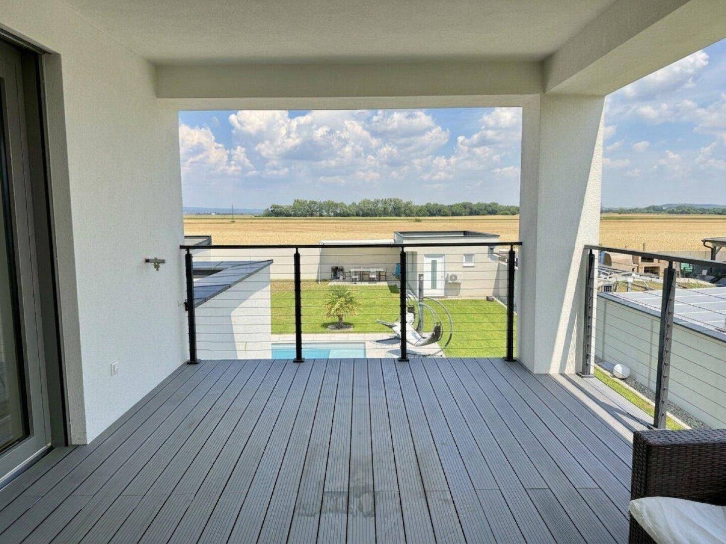 Geräumiger Balkon mit Holzdielenboden, Glasgeländer und weitem Blick über die Landschaft.