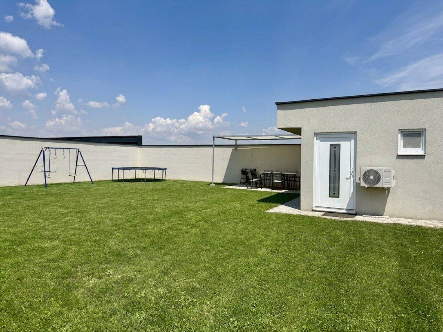 Großer Garten mit Rasenfläche, Schaukel und Trampolin für Kinder.
