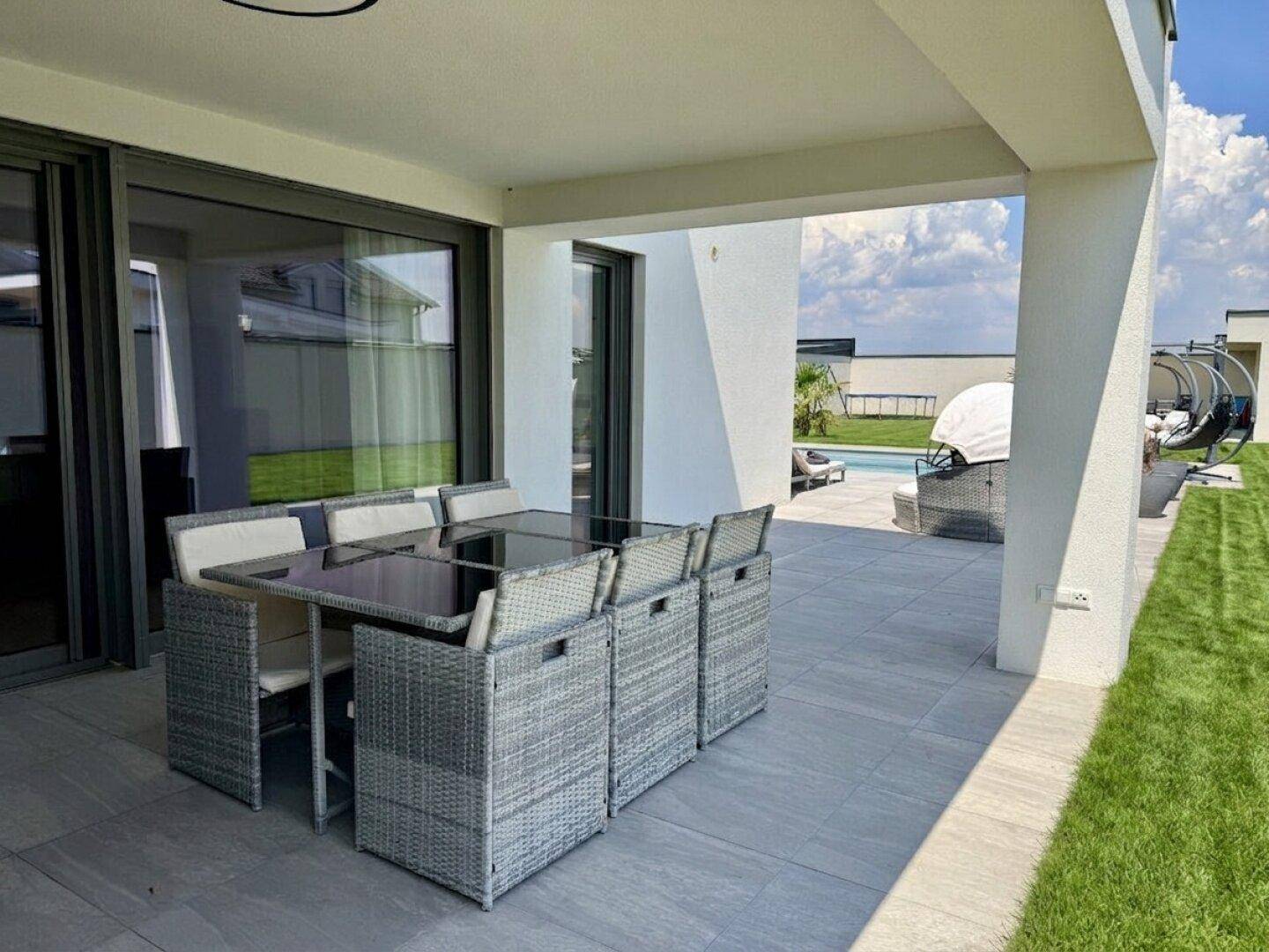 Geräumige überdachte Terrasse mit modernem Esstisch und Blick ins Grüne.