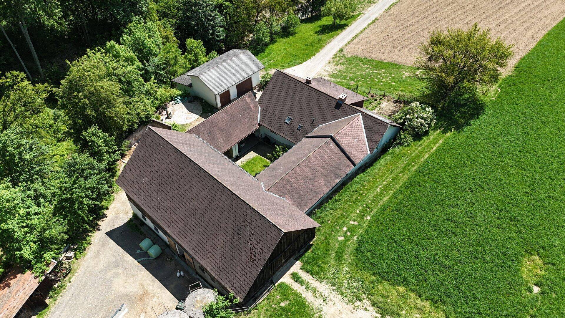 Ansicht von oben auf die Gebäudestruktur des Hofes, umgeben von Feldern und Wald.