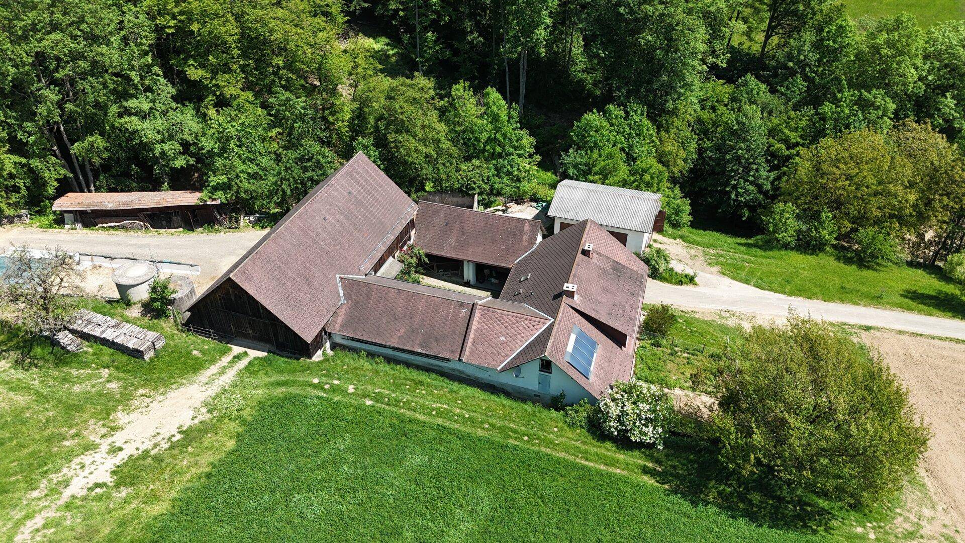 Vogelperspektive des Hofes, der von grünen Wiesen und Bäumen umgeben ist, mit mehreren Gebäuden.
