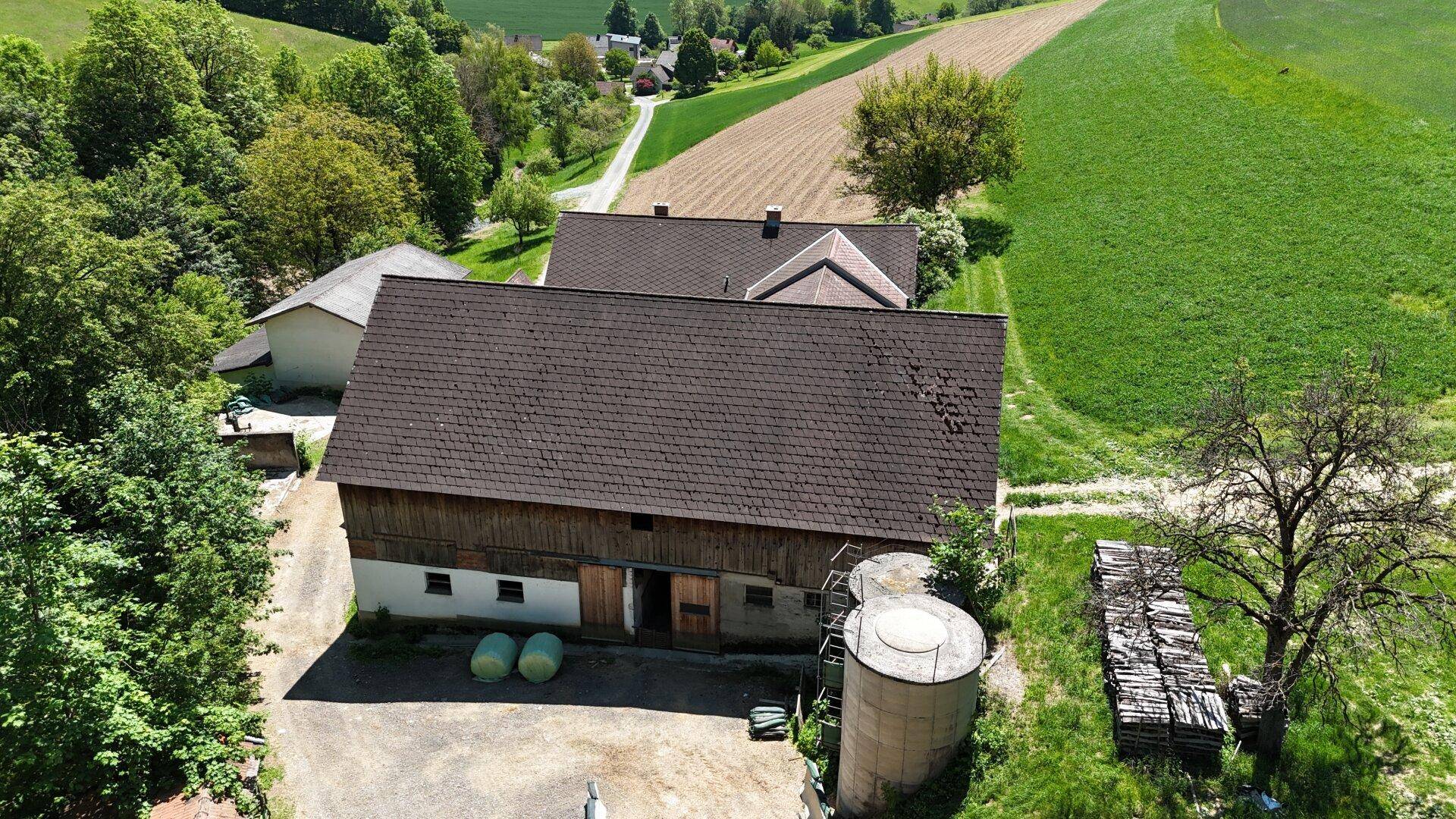 Ansicht eines landwirtschaftlichen Gebäudes mit Holzwänden und einem großen Dach, umgeben von Natur.
