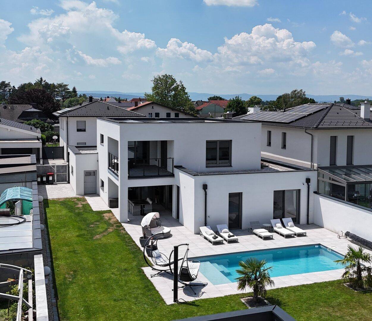 Luftaufnahme eines modernen Hauses mit Pool, großer Terrasse und gepflegtem Garten.