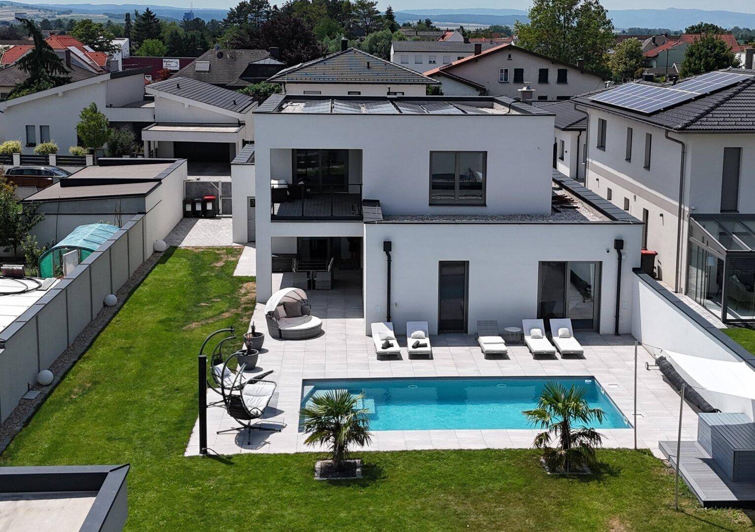 Luftaufnahme einer modernen Villa mit Pool, Garten und Photovoltaikanlage auf dem Flachdach.