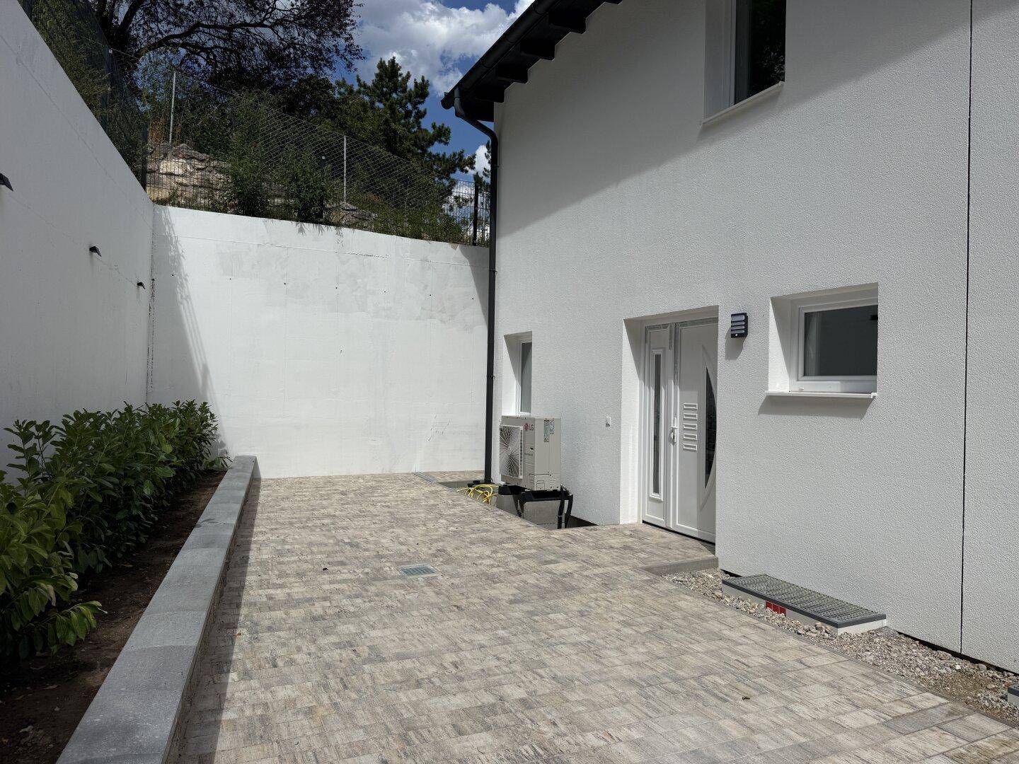 Seitenansicht des Hauses mit gepflastertem Bereich und Wärmepumpenanlage.