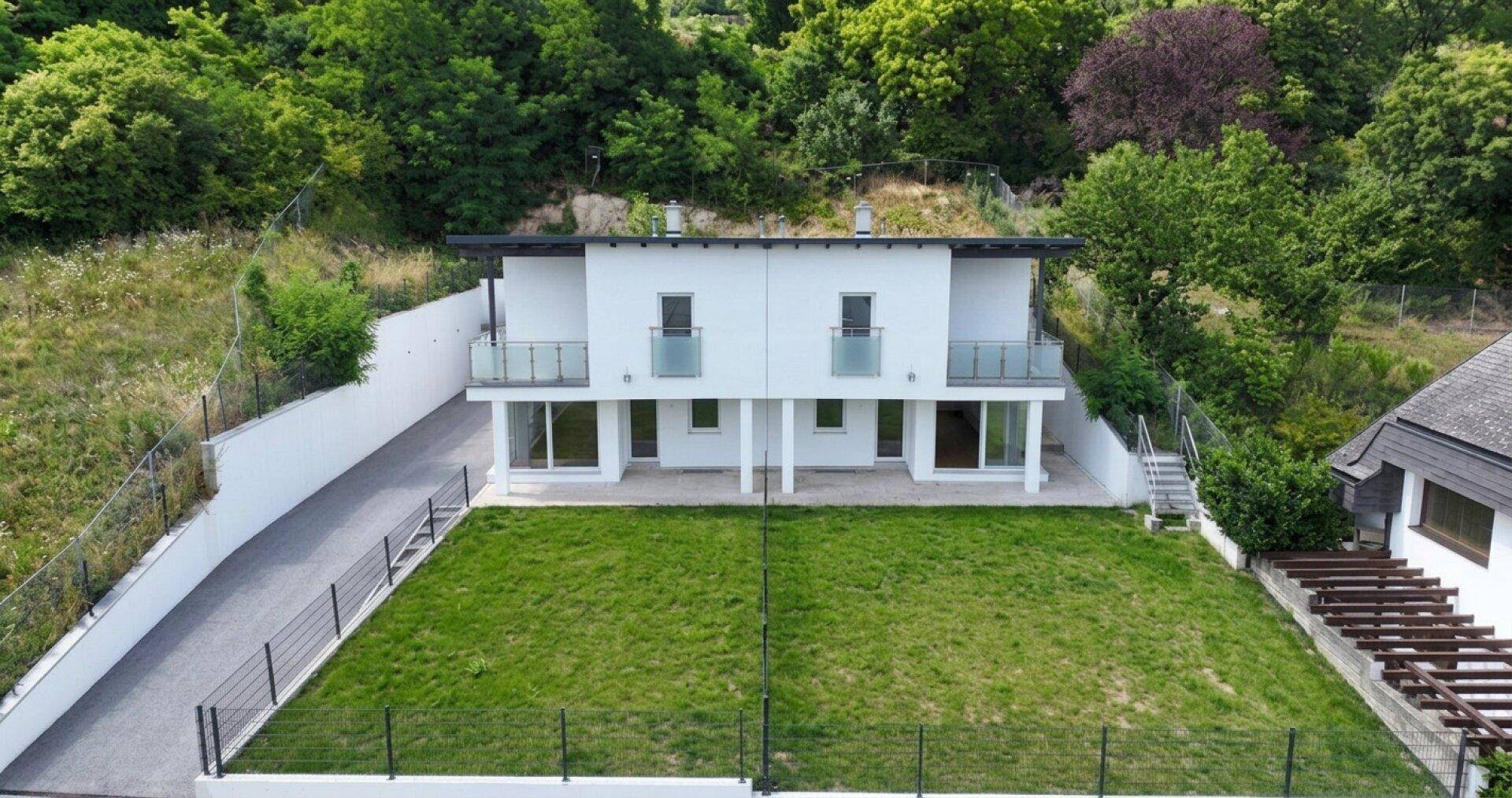 Luftaufnahme eines modernen Hauses mit großem Garten und umgebender Naturlandschaft.