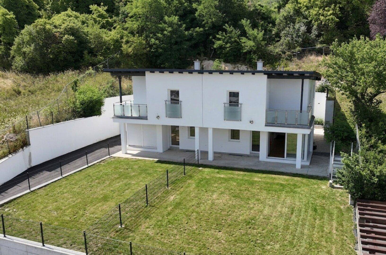 Vogelperspektive eines modernen Hauses mit Garten und umliegender grüner Hügellandschaft.