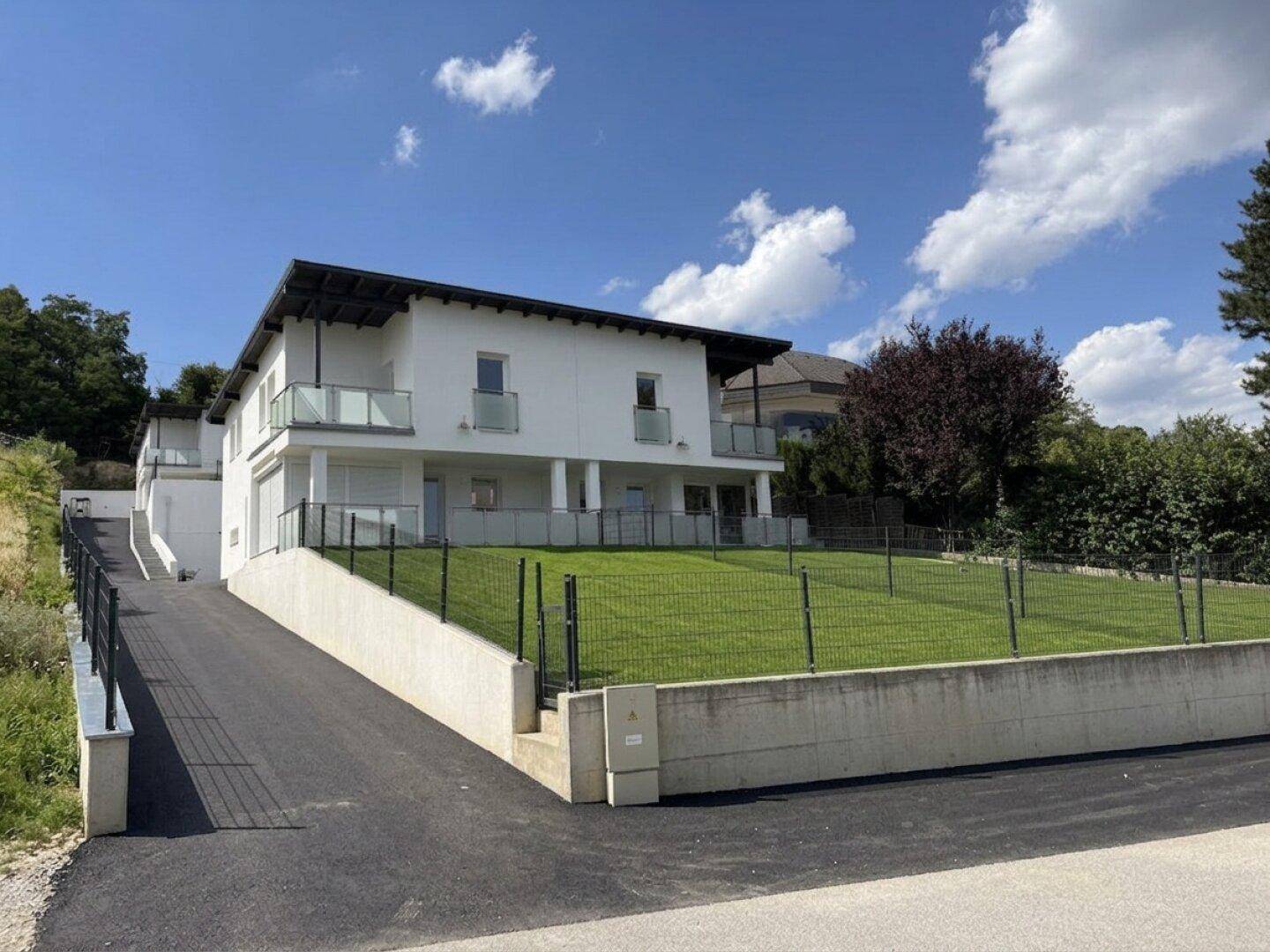 Modernes Einfamilienhaus mit Zufahrt, Garten und Blick auf die Umgebung.