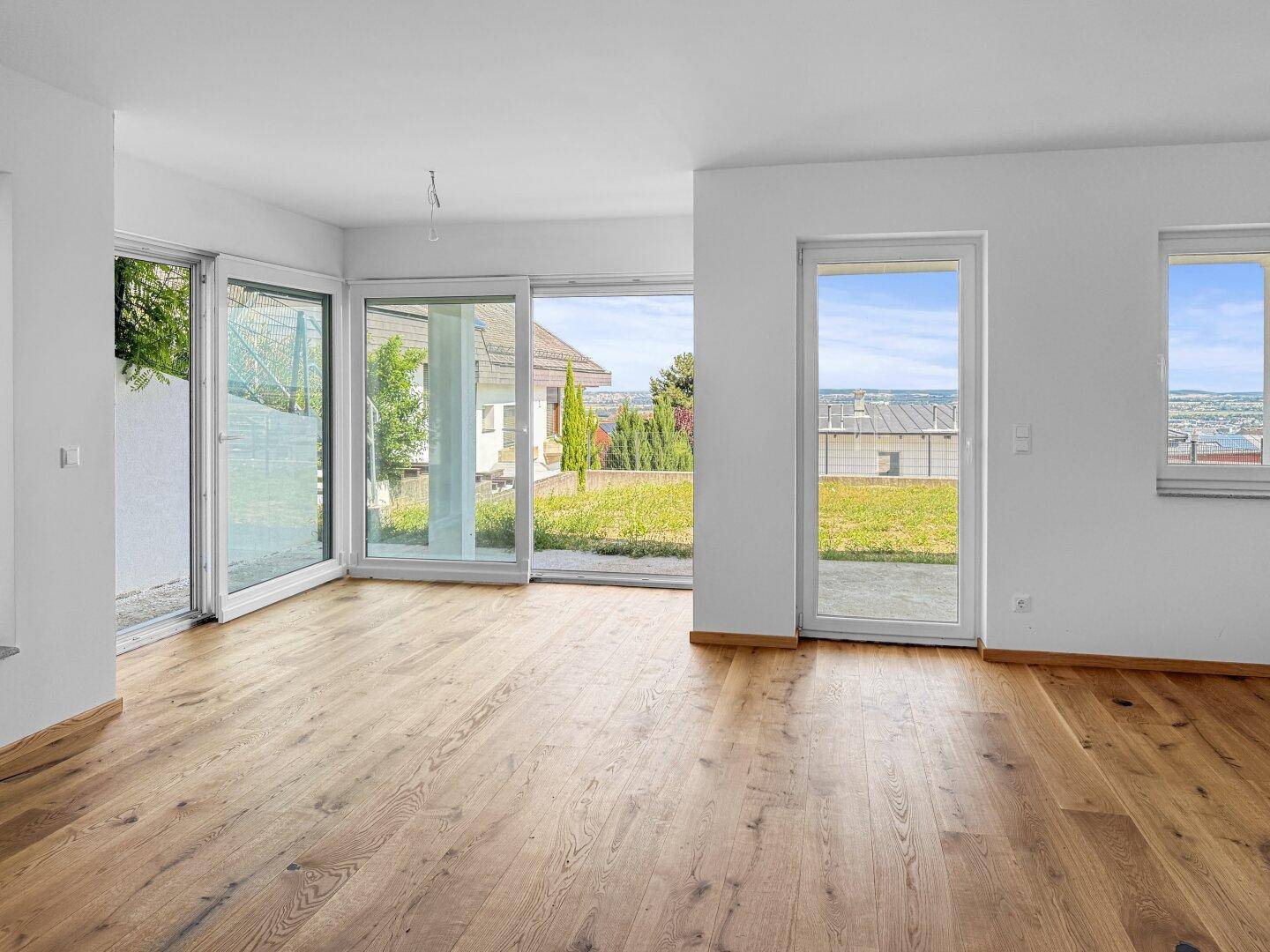 Heller Wohnbereich mit großen Fenstern, Holzboden und Zugang zum Garten.