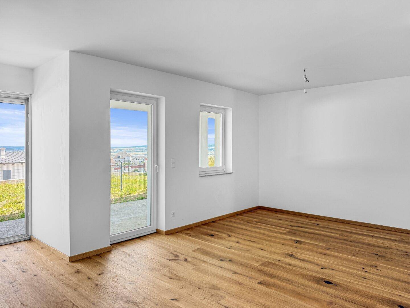 Heller Raum mit Holzboden und großer Fenstertür, die viel Tageslicht hereinlässt.