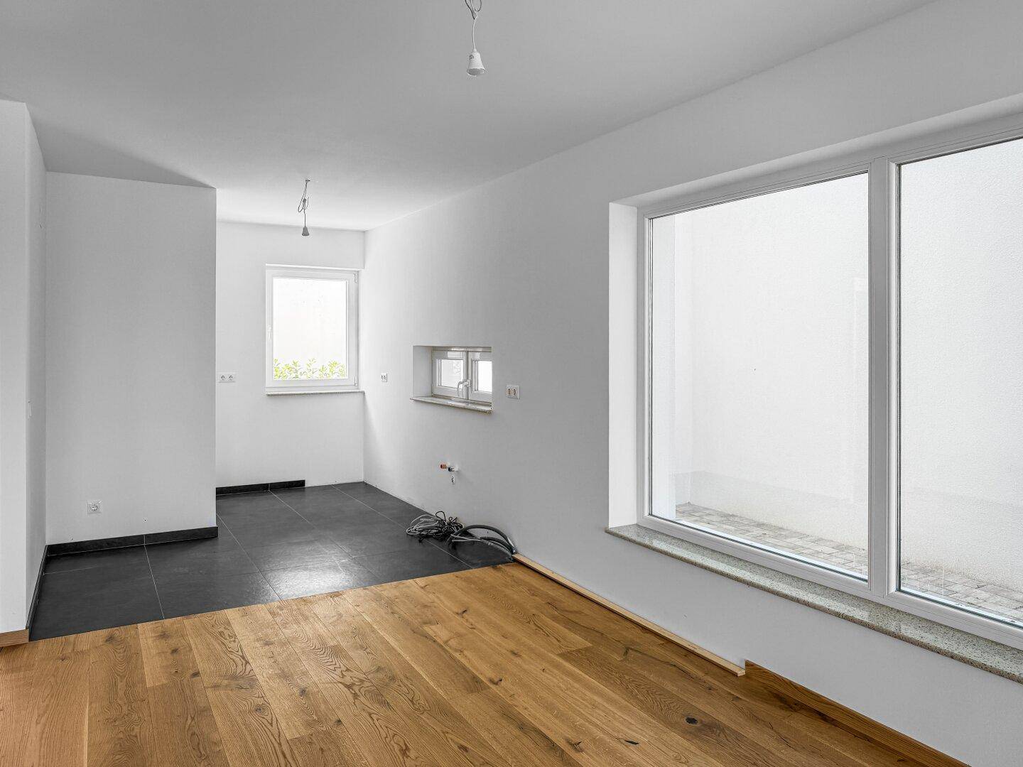 Leerer Küchenbereich mit dunklen Fliesen, Holzboden und Fenster zum Innenhof.