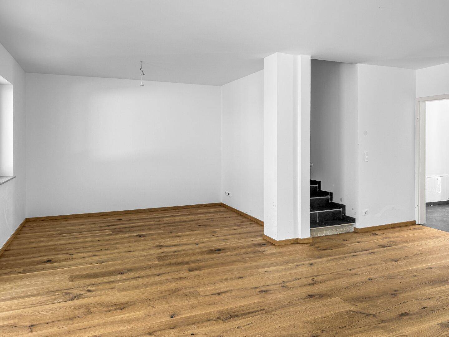 Offener Wohnbereich mit Holzboden, weiß gestrichenen Wänden und Treppenaufgang.