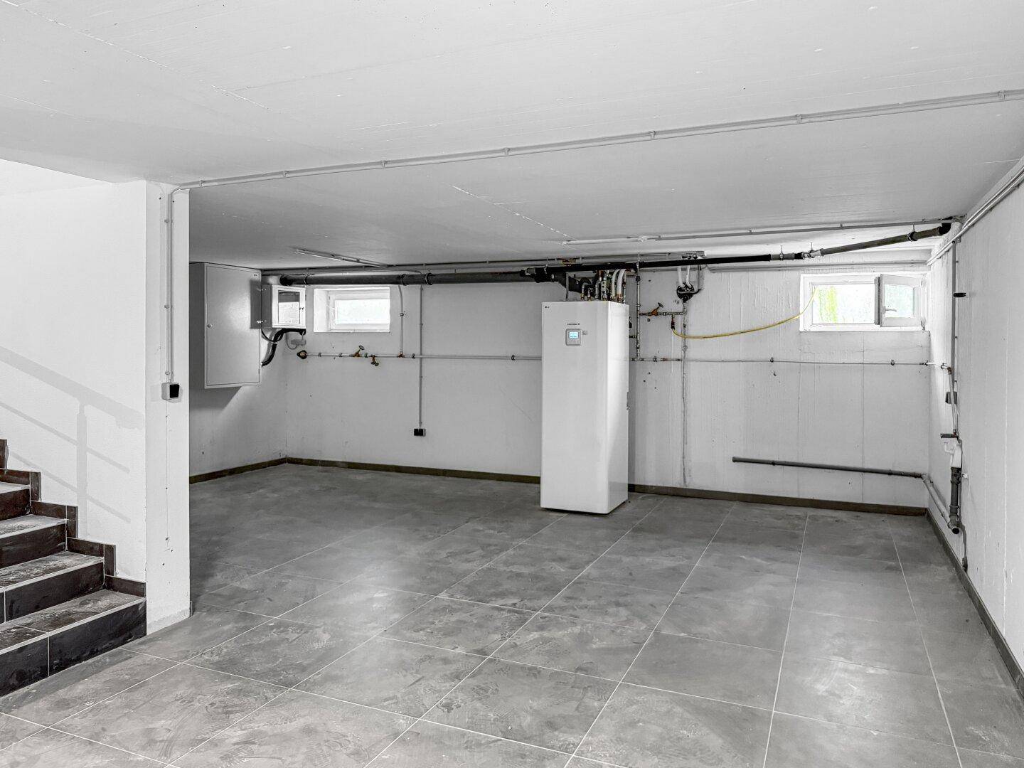 Funktionaler Kellerraum mit Fliesenboden, Heizungsanlage und kleinen Fenstern.
