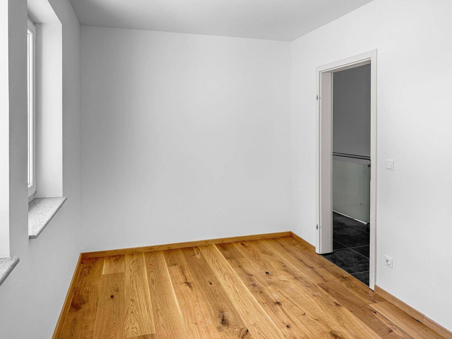 Helles Schlafzimmer mit Holzboden und Fenster, bereit zur individuellen Gestaltung.