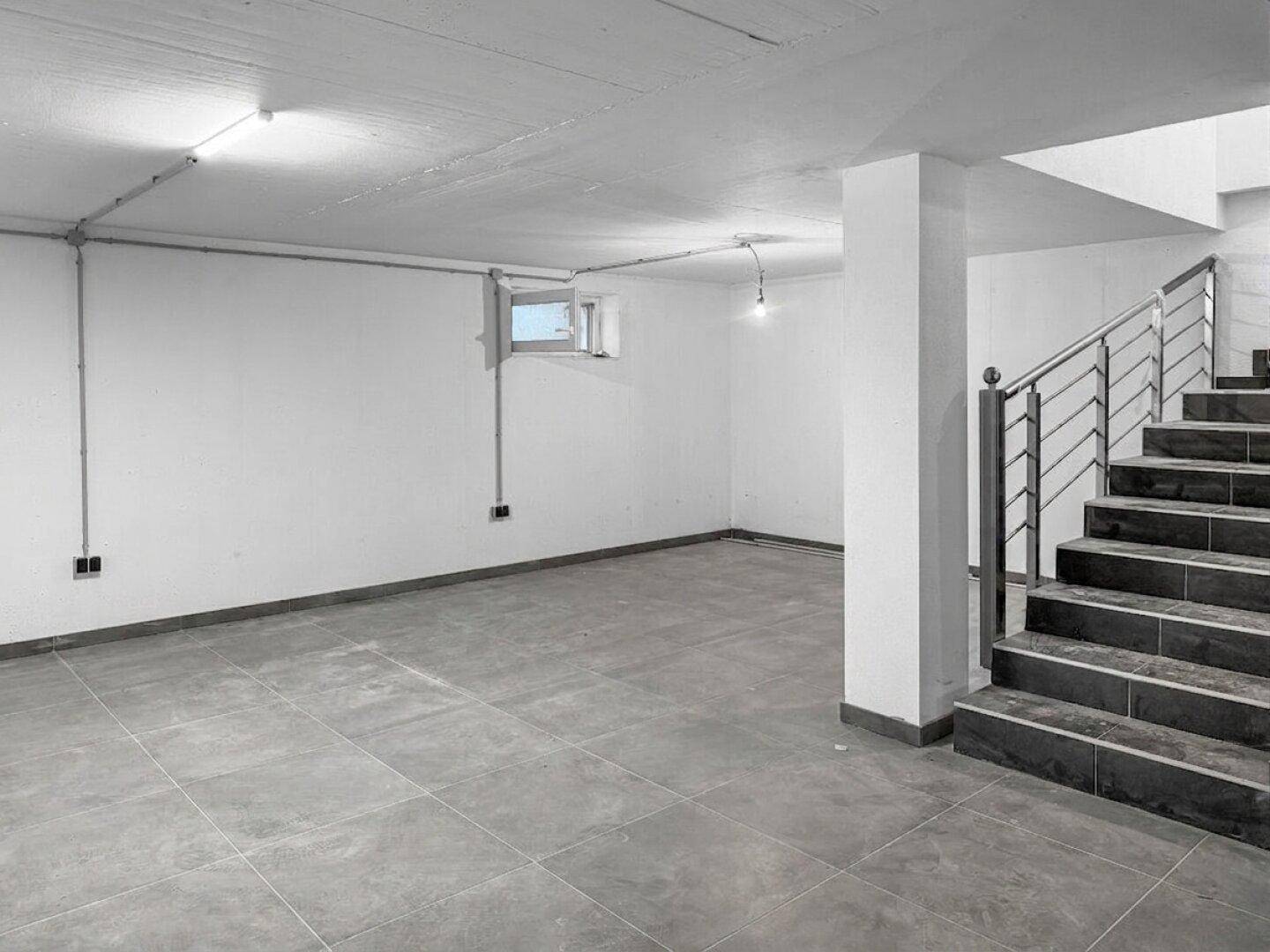 Heller Kellerraum mit Fliesenboden, kleinem Fenster und Zugang zur Treppe.