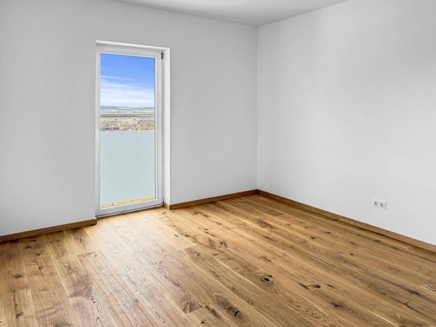 Helles Zimmer mit Holzboden und Fenstertür, die Zugang zu einem Außenbereich bietet.